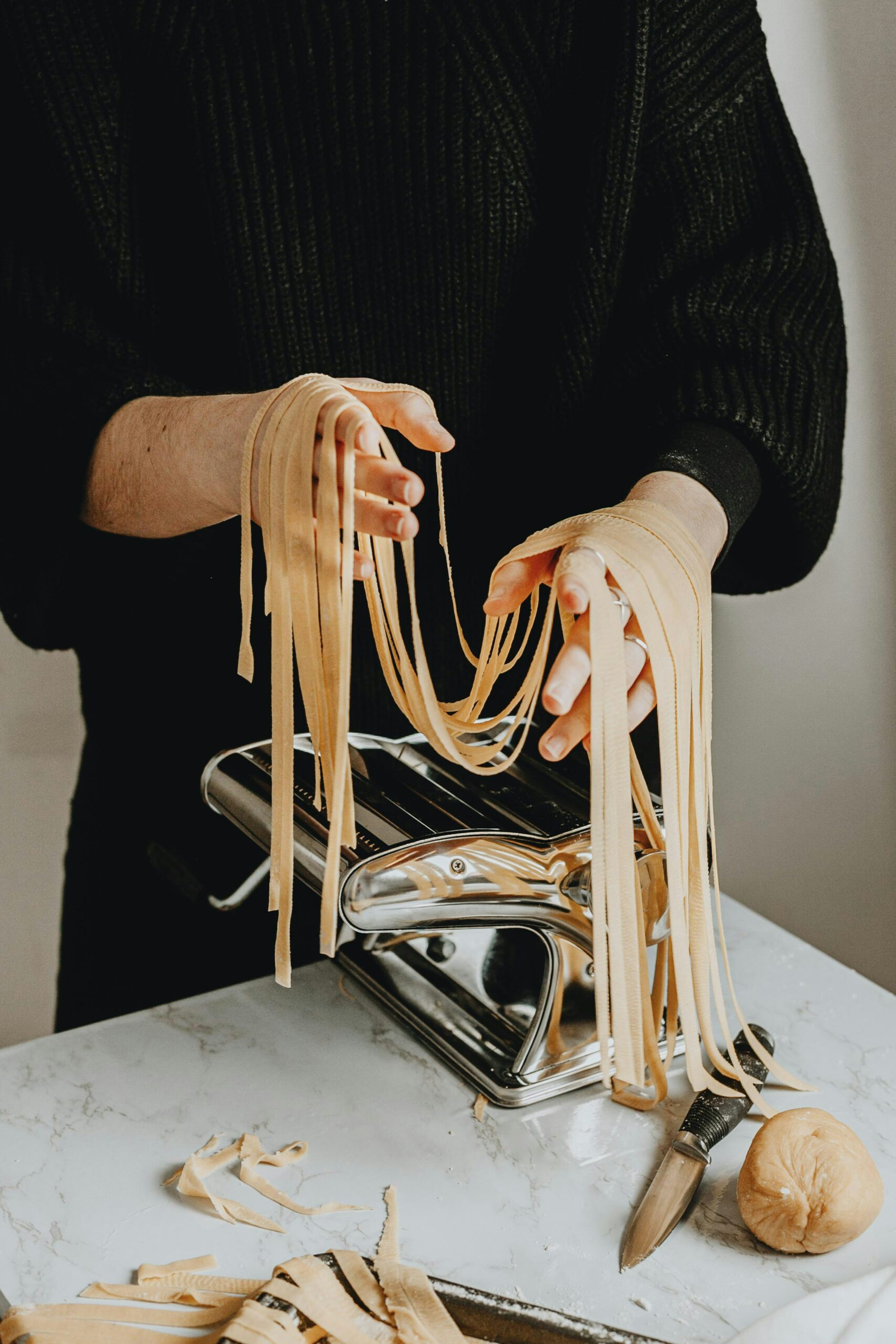 Bild von Tagliatelle-Nudeln neben einer Nudelmaschine.