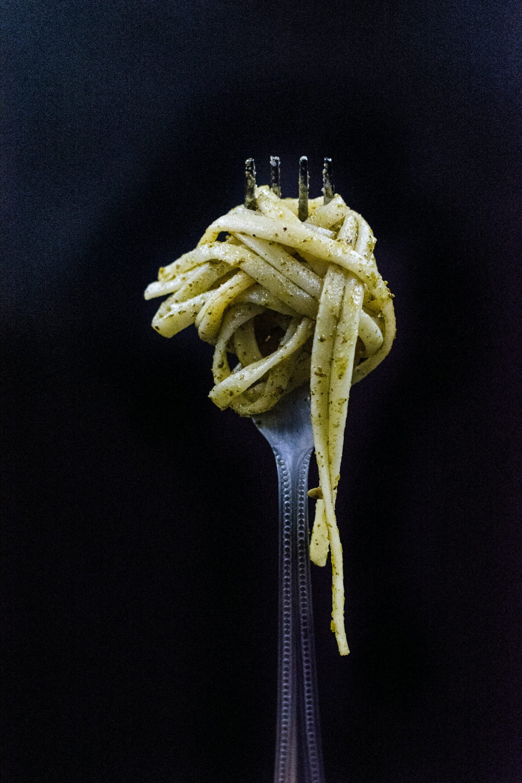Bild von einer Gabel, die mit frisch zubereiteter Pasta al pesto beladen ist.